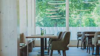 Helles, modernes Restaurant mit Holzverkleidung, bequemen Sitzmöbeln und großflächigen Fenstern mit Blick ins Grüne