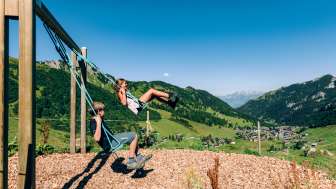 Zwei Kinder schaukeln mit der Aussicht auf Malbun