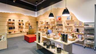 Helles Besucherzentrum mit modernen Holzregalen, gefüllt mit Souvenirs, Spezialitäten und Informationsmaterialien