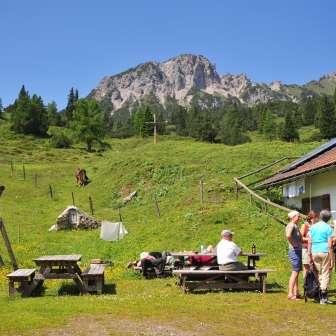 Blick auf die Berge von der Alpe Guschg an der mehrere Personen Pause machen und genießen