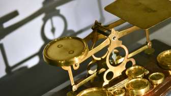 Bild einer antiken goldfarbenen Balkenwaage mit verschiedenen Gewichten, ausgestellt im Liechtensteinischen PostMuseum