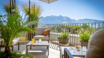 Sonnige Terrasse mit modernen Loungemöbeln und Alpenpanorama im Hintergrund