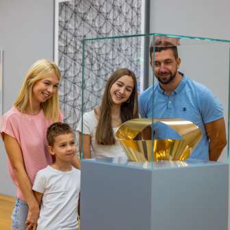Familie mit zwei Kindern betrachtet eine gläserne Vitrine mit goldener Skulptur im Museum