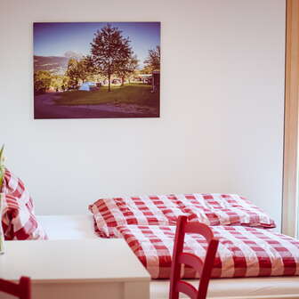 Gemütliches Doppelzimmer im Gästehaus beim Camping Mittagsspitze mit rot-weiß karierter Bettwäsche und Dekoration.