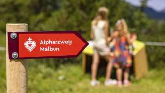 Signpost of the Malbun Alpine Heart Trail with children in front of one of the stations in the background