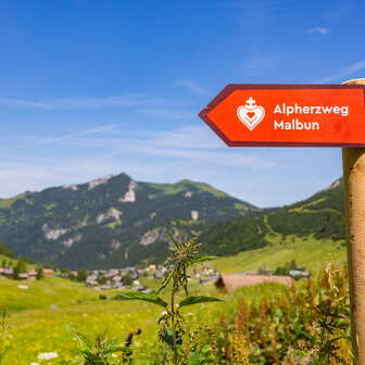 Wegweiser des Alpherzwegs mit Bergdorf Malbun im Hintergrund