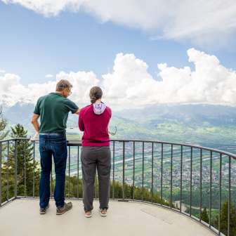 Zwei Personen genießen die Aussicht vom Aussichtspunkt Gaflei über das Rheintal in Liechtenstein bei klarem Wetter.