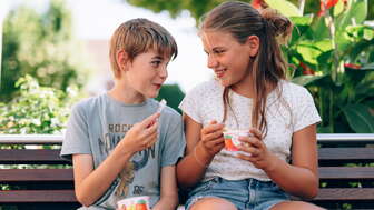 Two children enjoying an ice cream on a wooden bench in front of the ice cream parlor