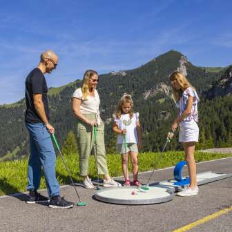 Family playing mini golf together in the mountains of Malbun in bright sunshine