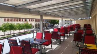 Sonnige Terrasse mit roten Stühlen und weiss gedeckten Tischen