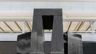 Skulptur „Progression einer Form in 3 Stelen“ von Christian Megert aus schwarzem Stein vor moderner Glasfassade in Vaduz.