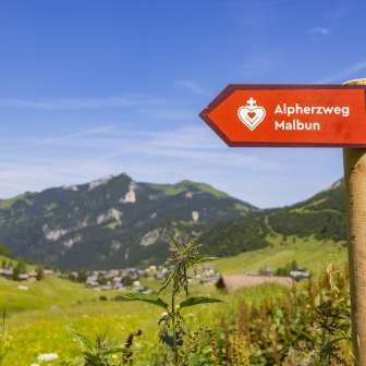 Signpost of the Alpherzweg with the mountain village of Malbun in the background