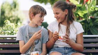 Two children enjoying an ice cream on a wooden bench in front of the ice cream parlor