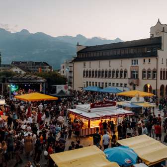 Vaduz City Hall at dusk with fairy lights, children playing on a table tennis table and a summery atmosphere on the state holiday