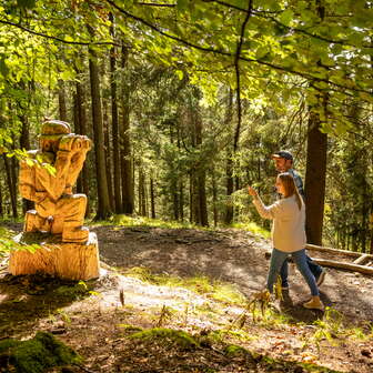 Zwei Wanderer laufen an einer Holzfigur auf dem WalserSagenWeg vorbei