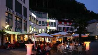 Abendliche Stimmung vor der Brasserie Burg in Vaduz mit beleuchteter Terrasse und Gästen unter Sonnenschirmen.