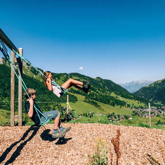 Zwei Kinder schaukeln mit der Aussicht auf Malbun
